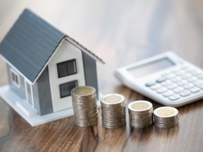 Kunststoffhaus neben steigenden Stapeln von 2 Euro Münzen und einem Taschenrechner im Hintergrund: Profitieren Sie von unseren vorteilhaften Baufinanzierungen mit einer breiten Auswahl an Anbietern.