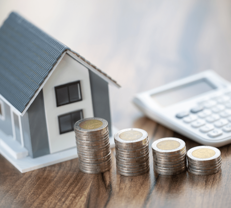 Kunststoffhaus neben steigenden Stapeln von 2 Euro Münzen und einem Taschenrechner im Hintergrund: Profitieren Sie von unseren vorteilhaften Baufinanzierungen mit einer breiten Auswahl an Anbietern.
